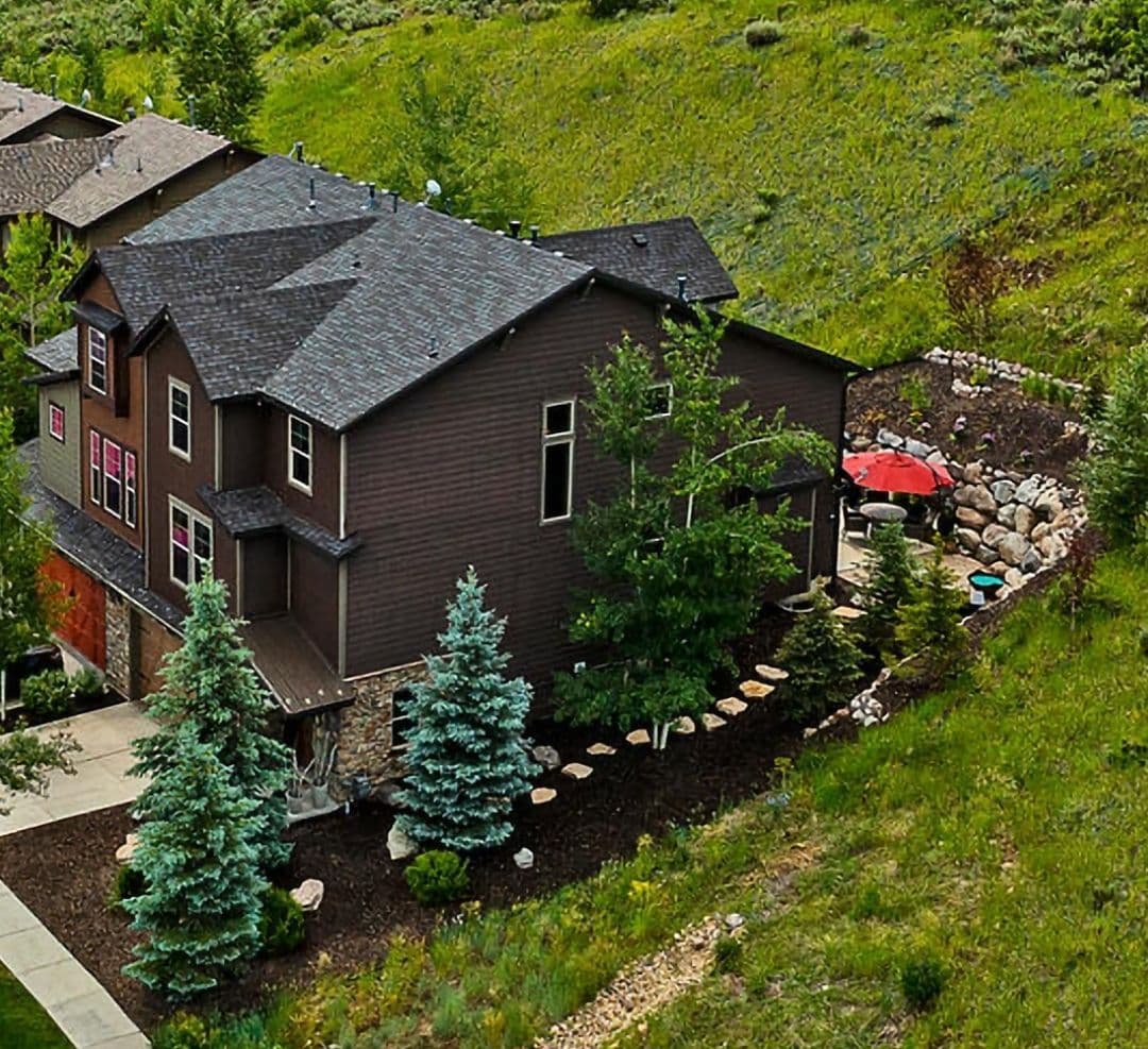 Aerial view of a modern home with lush landscaping and a patio featuring an umbrella.